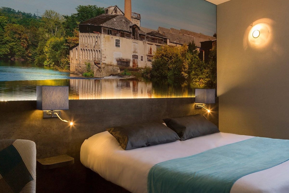Un dormitorio con cama, dos mesitas de noche, una lámpara de pared y un mural de un edificio y agua.