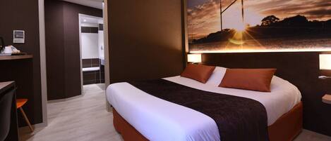 Habitación de hotel con una cama grande, un escritorio y vistas a un paisaje al atardecer.