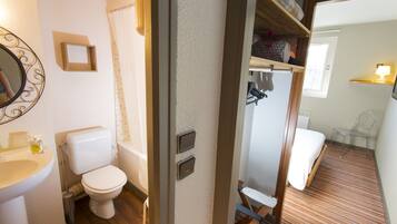 A bathroom with a toilet, sink, and shower. There is a mirror on the wall and a door leading to another room.