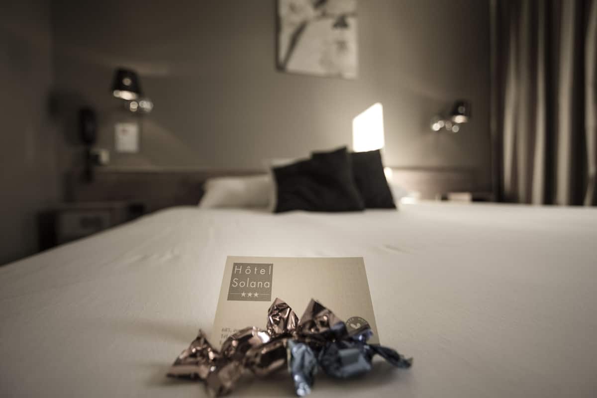 Una habitación de hotel con una cama bien hecha, una lámpara de noche y una tarjeta sobre la cama.