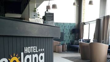 Un espace d’accueil avec une enseigne indiquant « HÔTEL Solana », un tapis à motifs et un coin salon avec un canapé et des fauteuils.