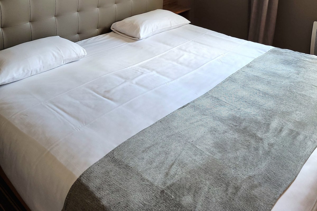 Una cama bien hecha con cabecera gris y ropa de cama blanca en una habitación de hotel.