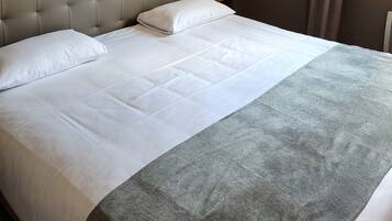 Een net opgemaakt bed met een grijs hoofdeinde en witte beddengoed in een hotelkamer.