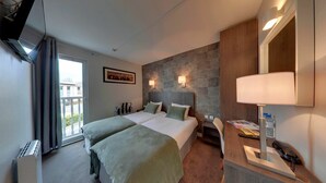 A hotel room with two beds, a stone accent wall, a large mirror, and a desk with a lamp. - Hotel Acadie Villebon-sur-Yvette (Villebon-sur-Yvette)