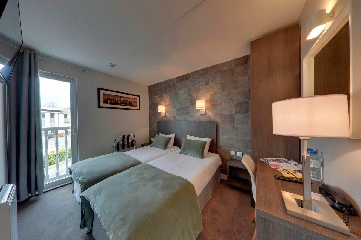 A hotel room with two beds, a stone accent wall, a large mirror, and a desk with a lamp.