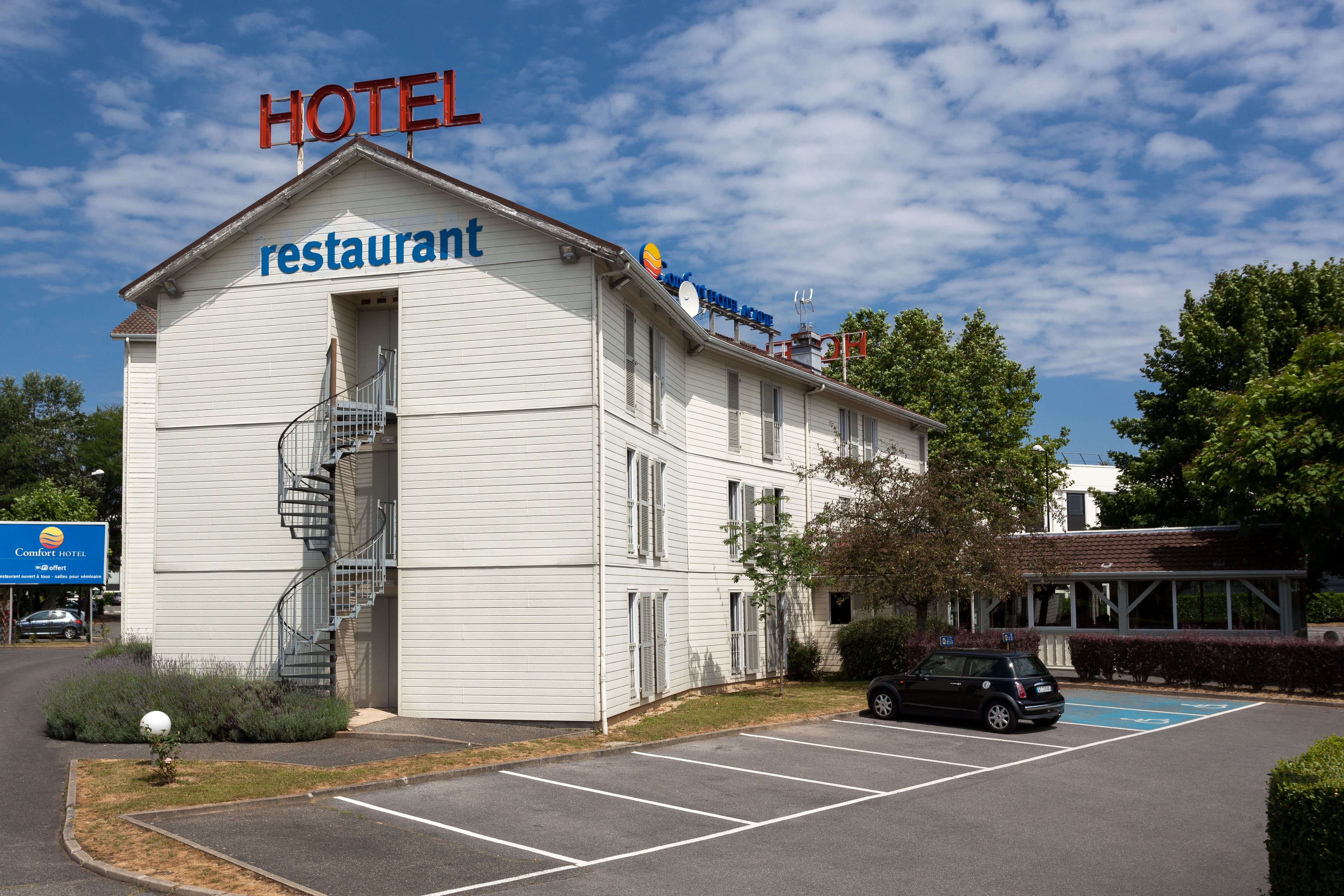 Un hotel con restaurante en la planta baja, aparcamiento y un cartel que indica un Comfort Hotel cercano.