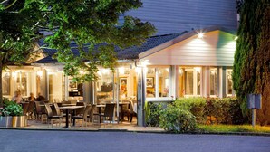 A restaurant with outdoor seating, a covered patio, and a well-lit entrance. - Hotel Acadie Villebon-sur-Yvette (Villebon-sur-Yvette)