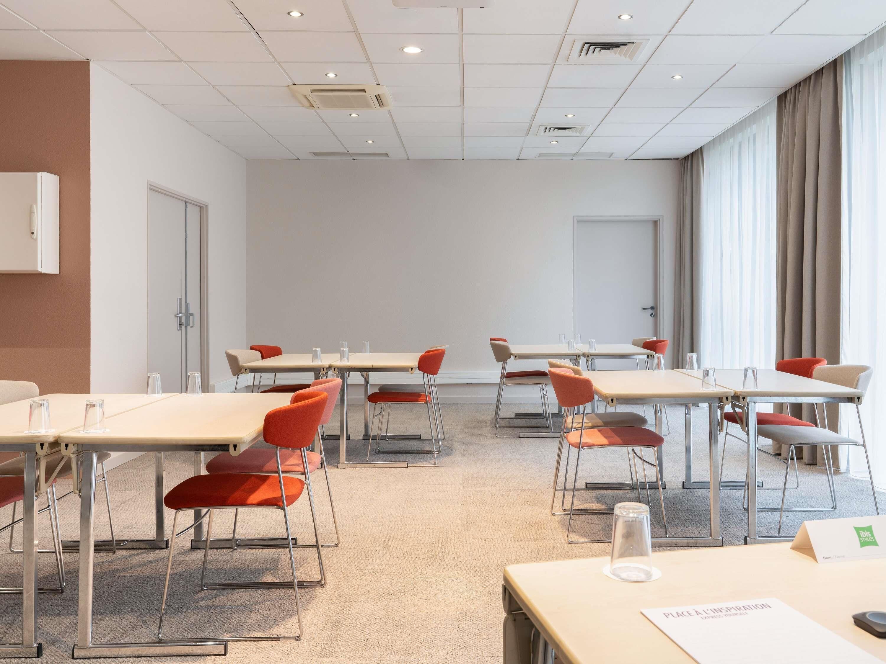 Un salón de conferencias con mesas, sillas y un amplio ventanal con cortinas.