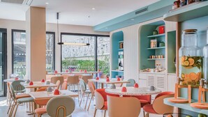 A modern cafe with round tables, chairs, and a large window. - ibis Styles Paris Porte d’Orléans Hotel (Montrouge)