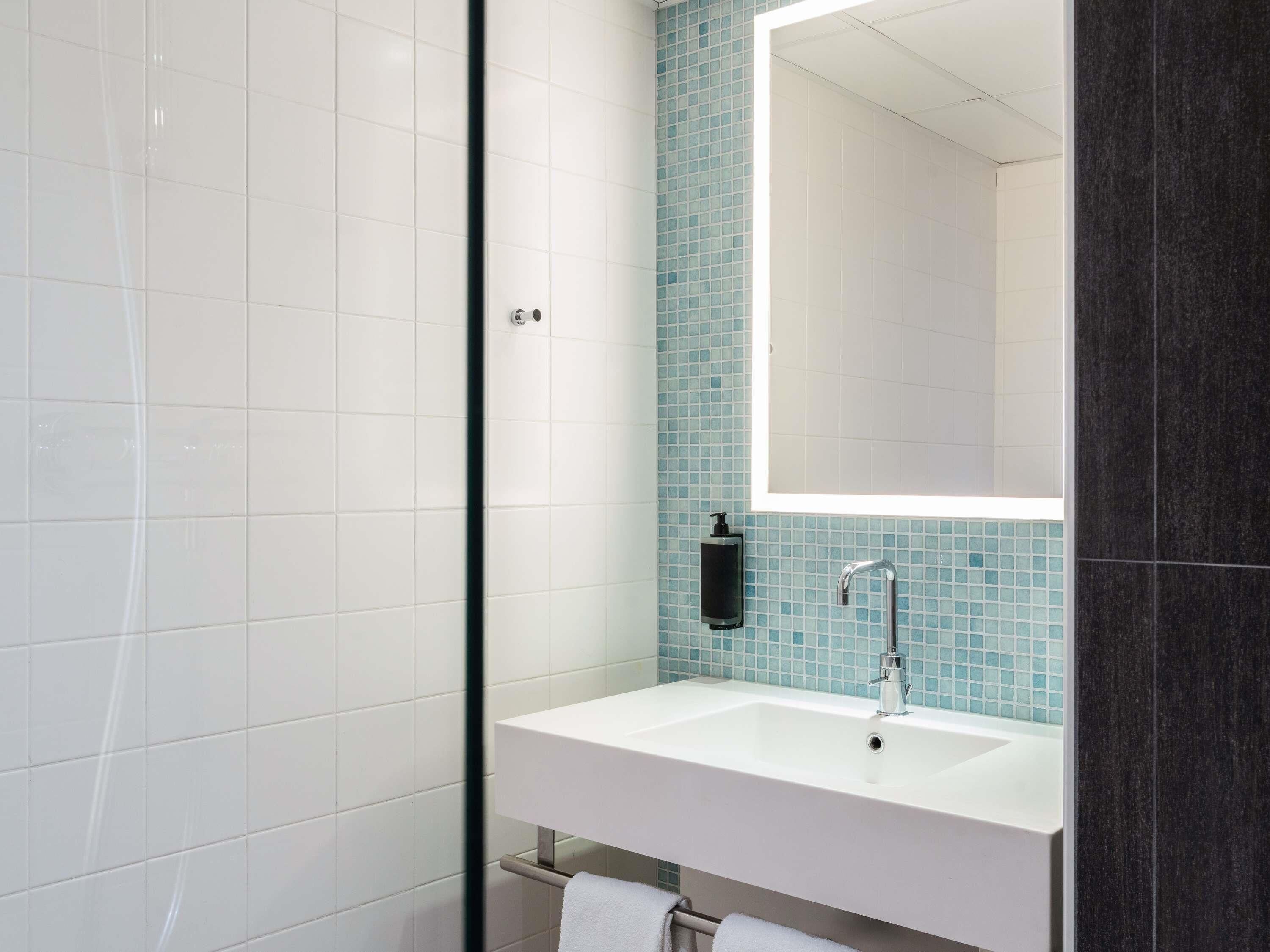 Une salle de bain moderne avec un lavabo blanc, un miroir et un espace douche.