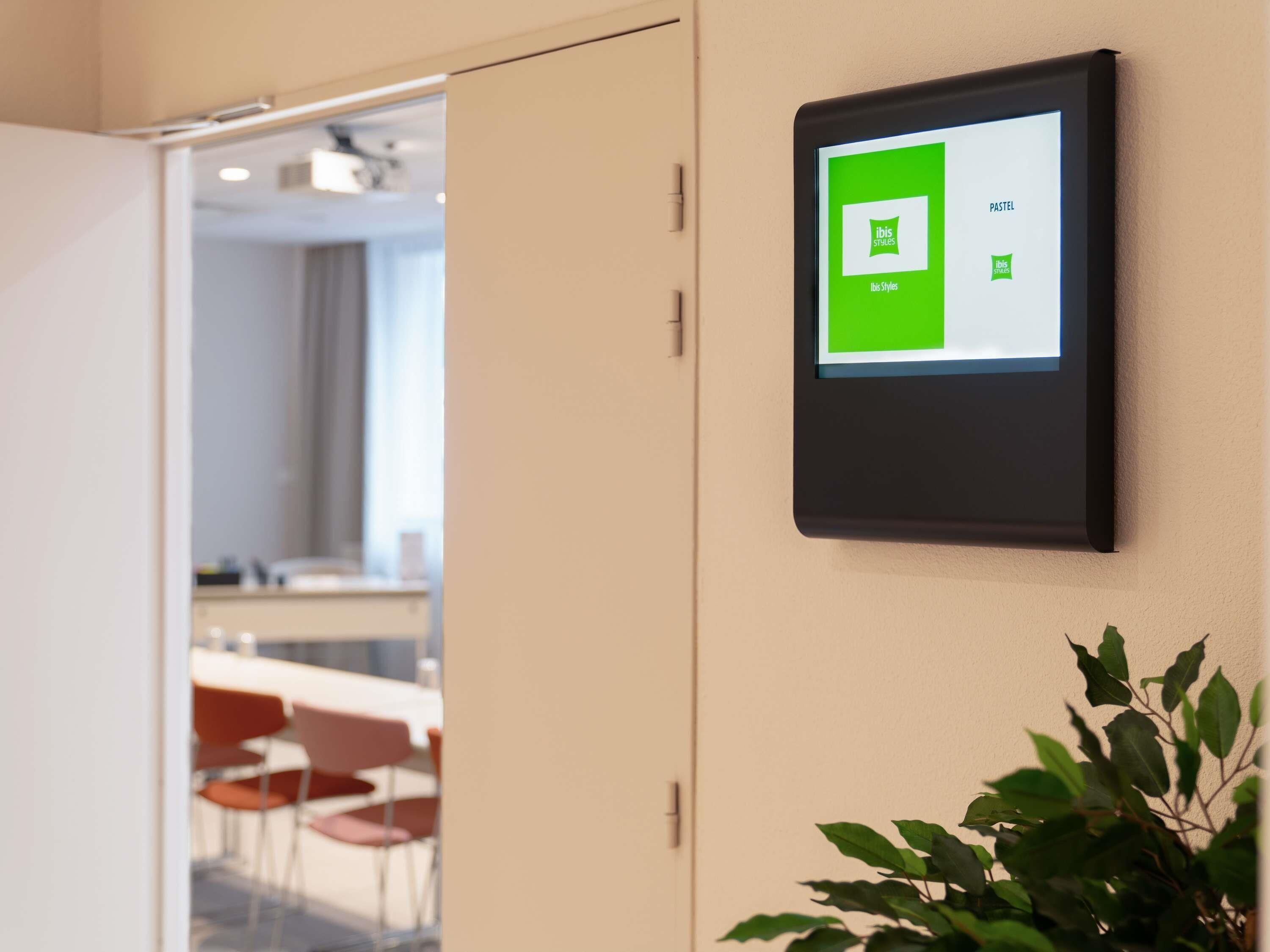 A digital display mounted on a wall with a plant below it.