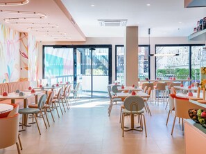 Interior moderno de restaurante com mesas e cadeiras, janelas amplas e arte colorida nas paredes.