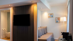 A modern hotel room with a bed, a sofa, a desk with a coffee maker, and a TV mounted on the wall. - ibis Styles Paris Porte d’Orléans Hotel (Montrouge)