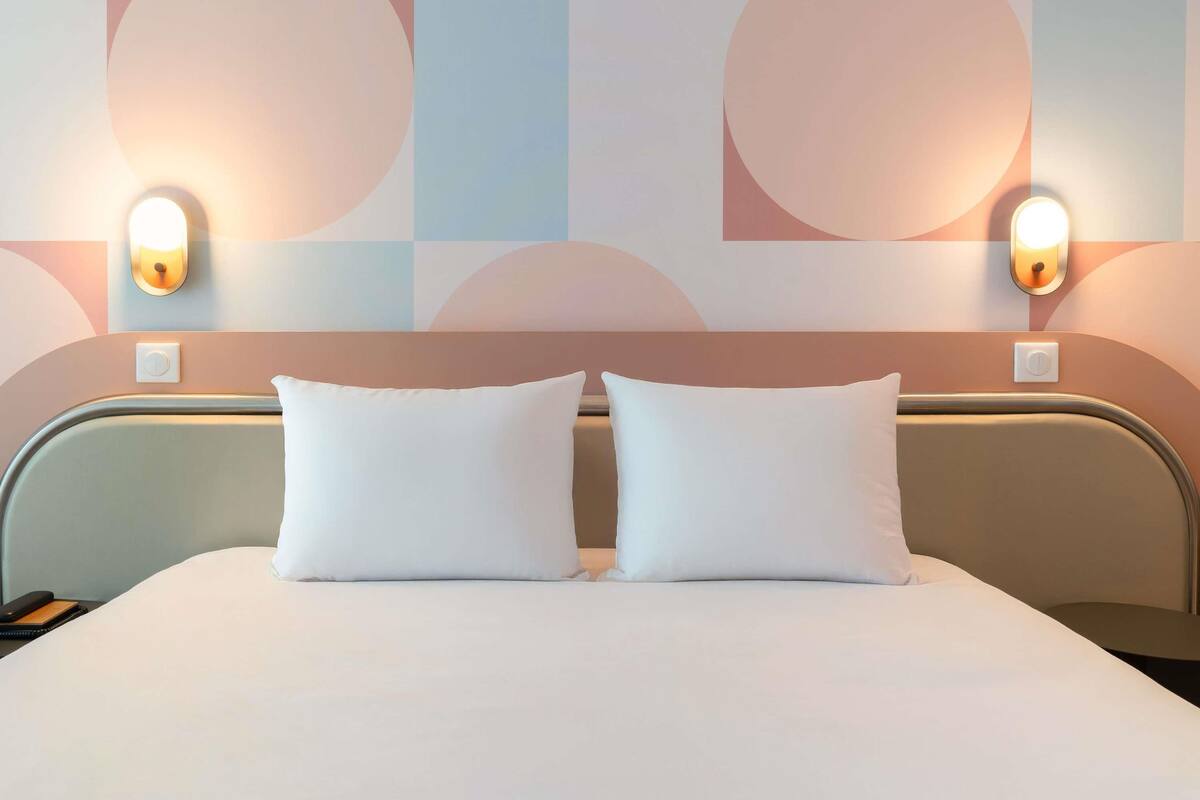 A hotel room with a bed, two bedside lamps, and a wall with abstract geometric patterns.