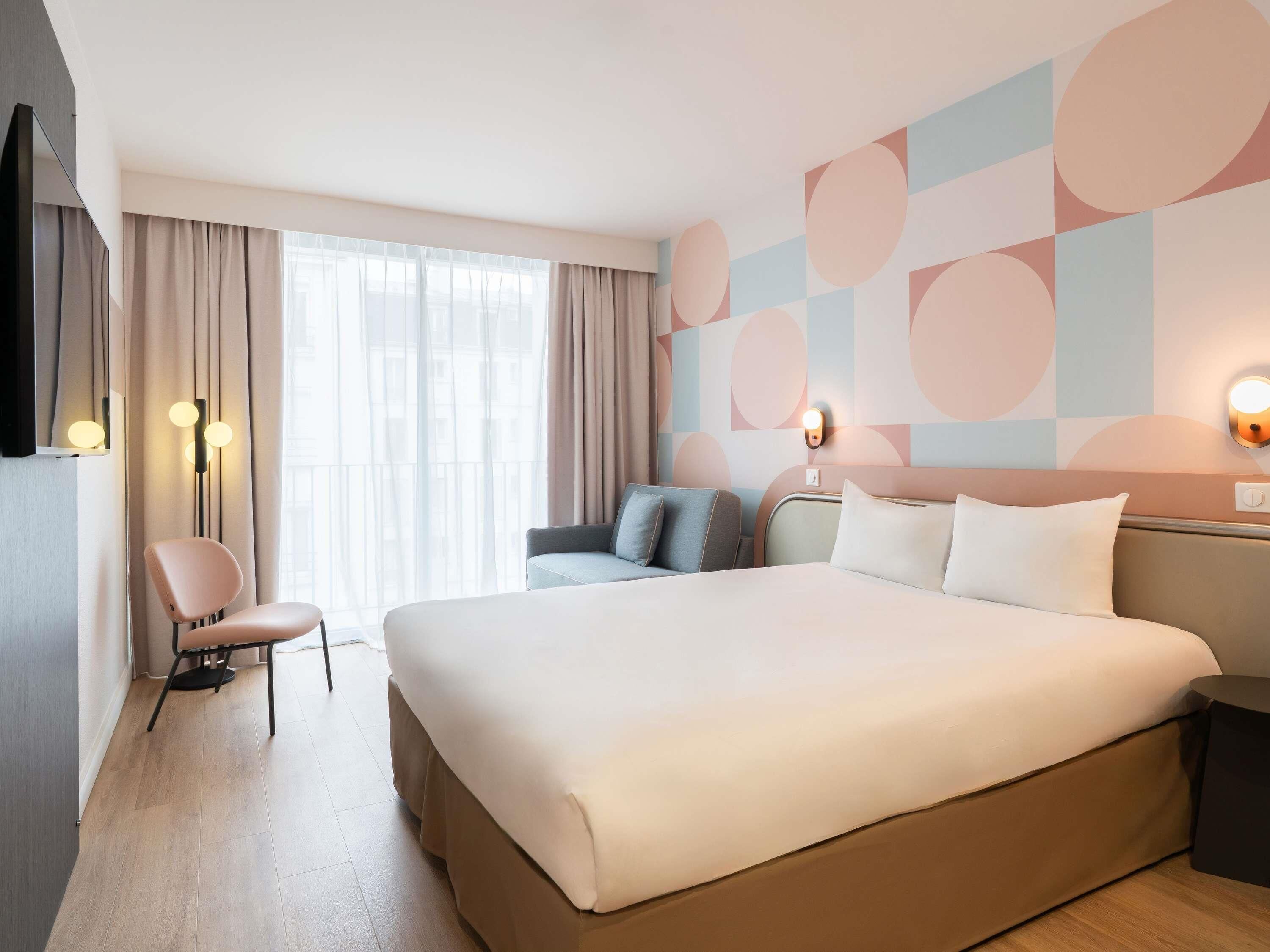 A hotel room with a large bed, a seating area with a chair, a sofa, and a wall-mounted light fixture.