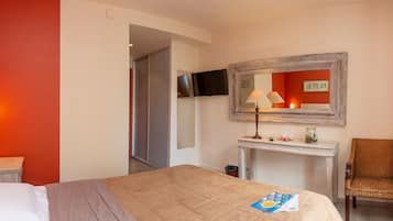 Habitación de hotel con una cama, un escritorio con lámpara, una silla y un espejo en la pared.