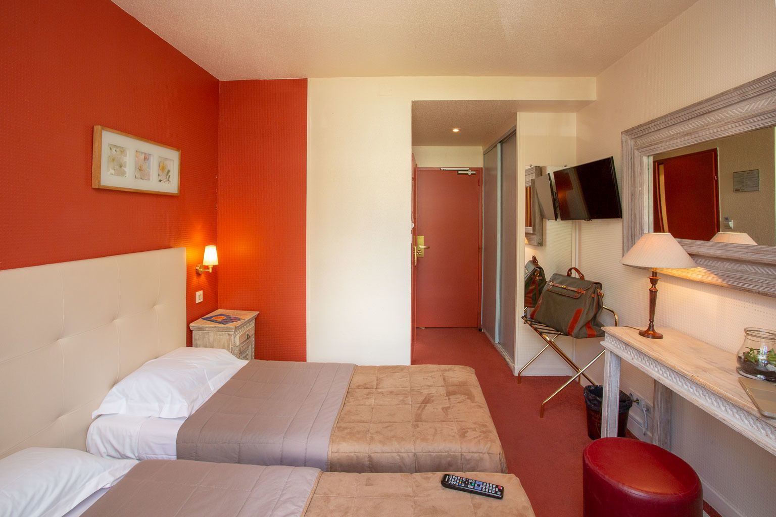 A hotel room with two beds, a TV, a mirror, and a desk with a lamp.