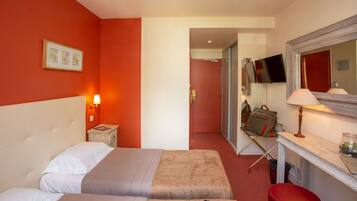 A hotel room with two beds, a TV, a mirror, and a desk with a lamp.