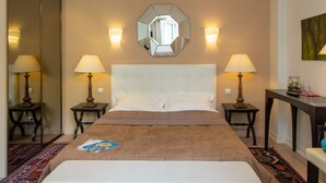 A hotel room with a large bed, two bedside lamps, a mirror above the bed, and a small table with a vase and glasses. - Hôtel Providence (Vittel)