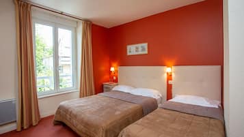 Une chambre d’hôtel avec deux lits, une fenêtre avec des rideaux, une lampe fixée au mur et un tableau encadré.