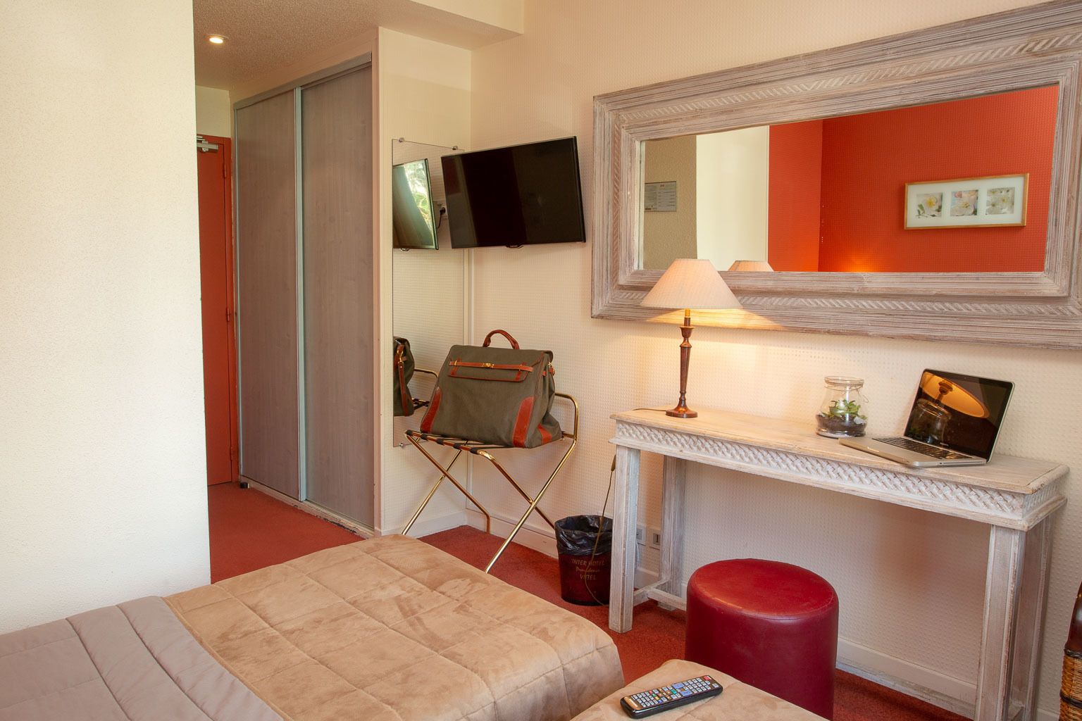 A hotel room with a bed, a desk with a lamp, a television, and a red wall.