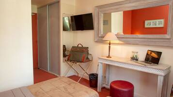 A hotel room with a bed, a desk with a lamp, a television, and a red wall.