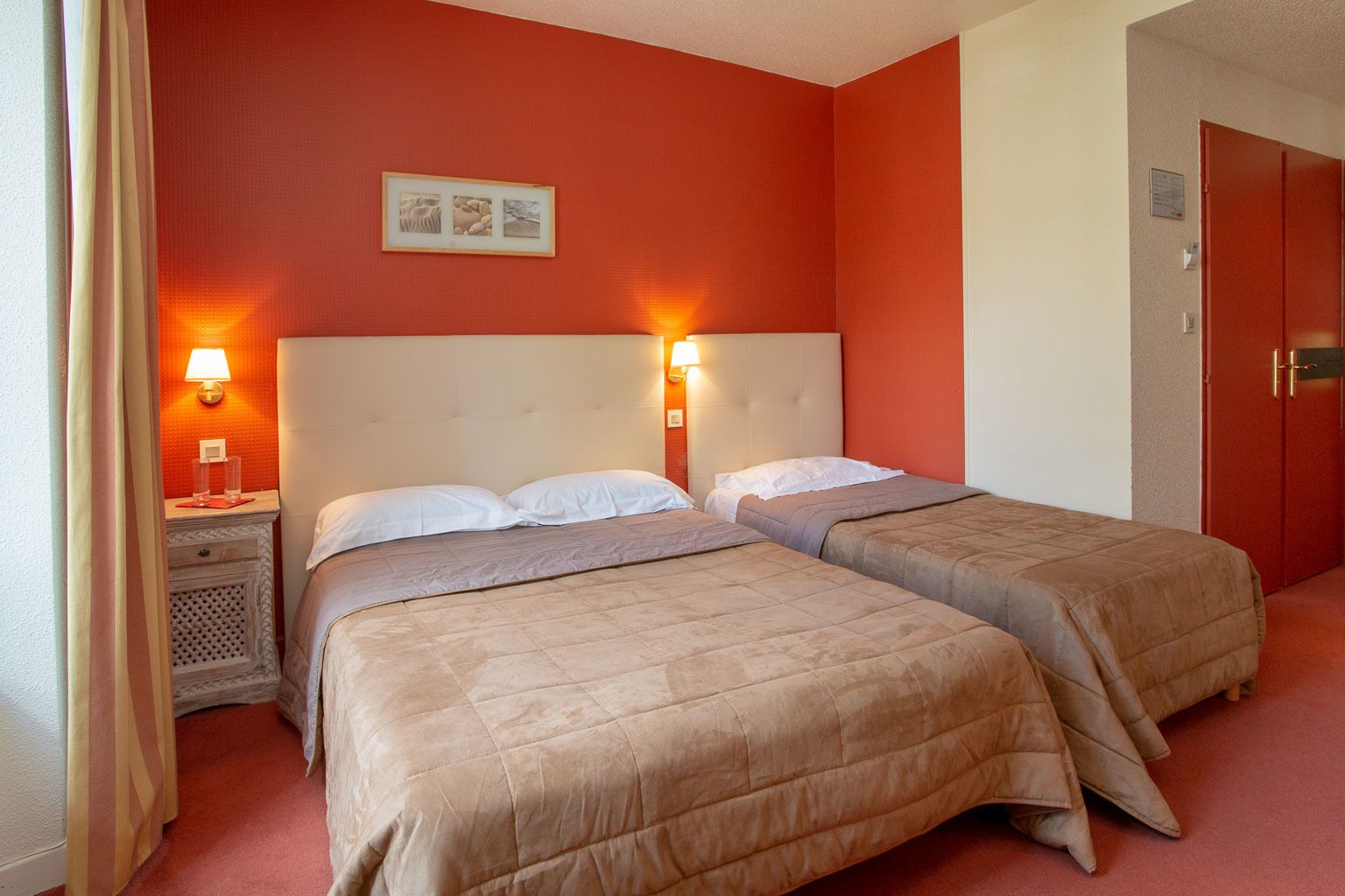 Ett hotellrum med två sängar, var och en med en sänggavel och sänglampor. Det finns ett litet bord med en lampa och en inramad tavla på väggen.