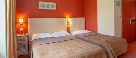 A hotel room with two beds, each with a headboard and bedside lamps. There is a small table with a lamp and a framed picture on the wall.