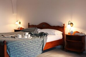 A neatly made bed with a floral bedspread, a tray of cups and a book on the nightstand, and two wall-mounted lamps. - Masseria Refrigerio (Ostuni)