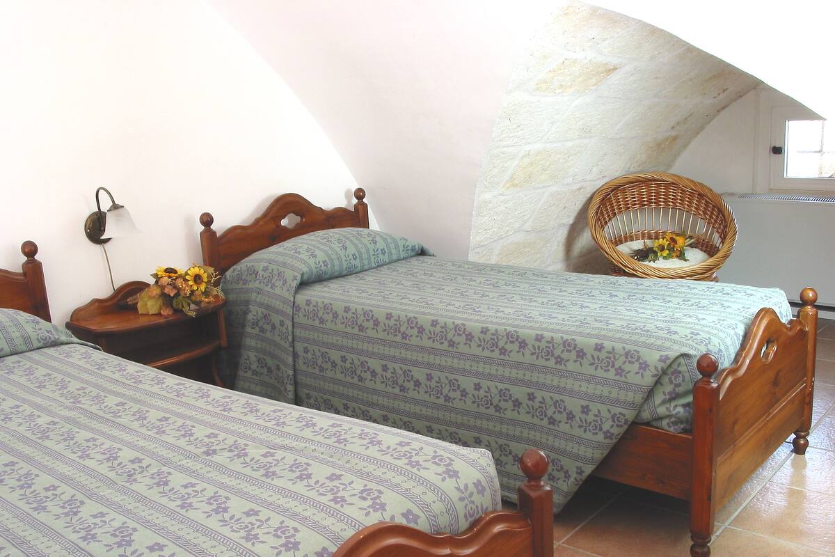 A bedroom with two wooden beds, a nightstand with a lamp, and a wicker chair.