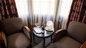 A room with two upholstered chairs, a small round table with a bottle of champagne, a glass, and a white bowl.