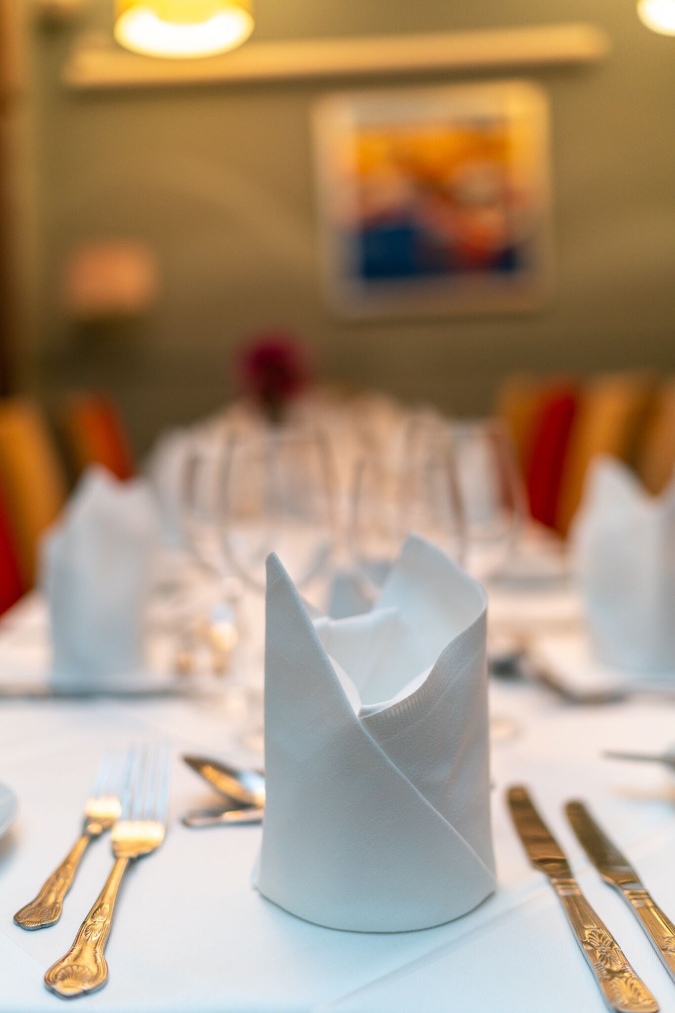 A table set with white napkins, gold cutlery, and a white napkin cone.