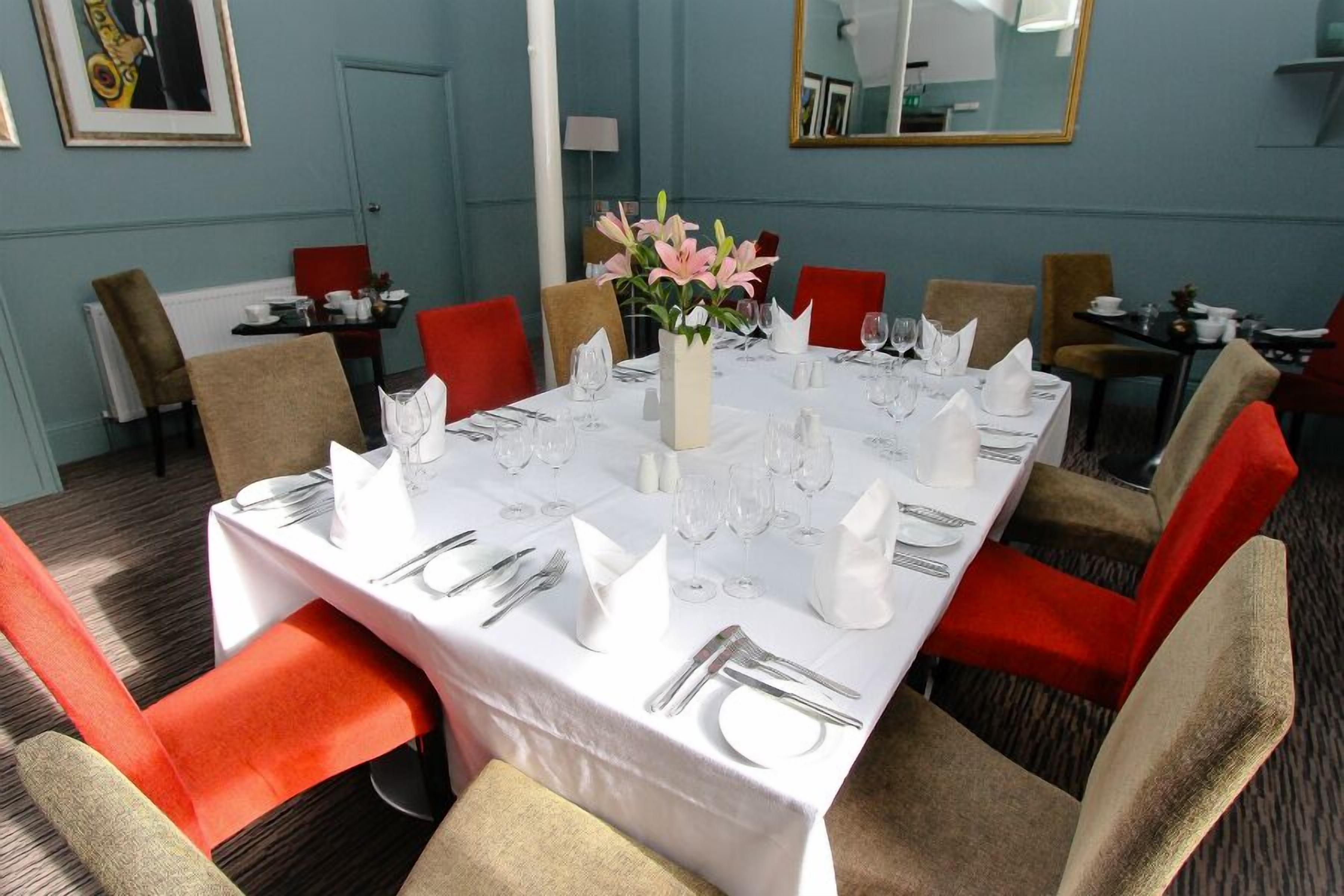 A dining area with a long table set for a meal, surrounded by chairs with red and beige upholstery.
