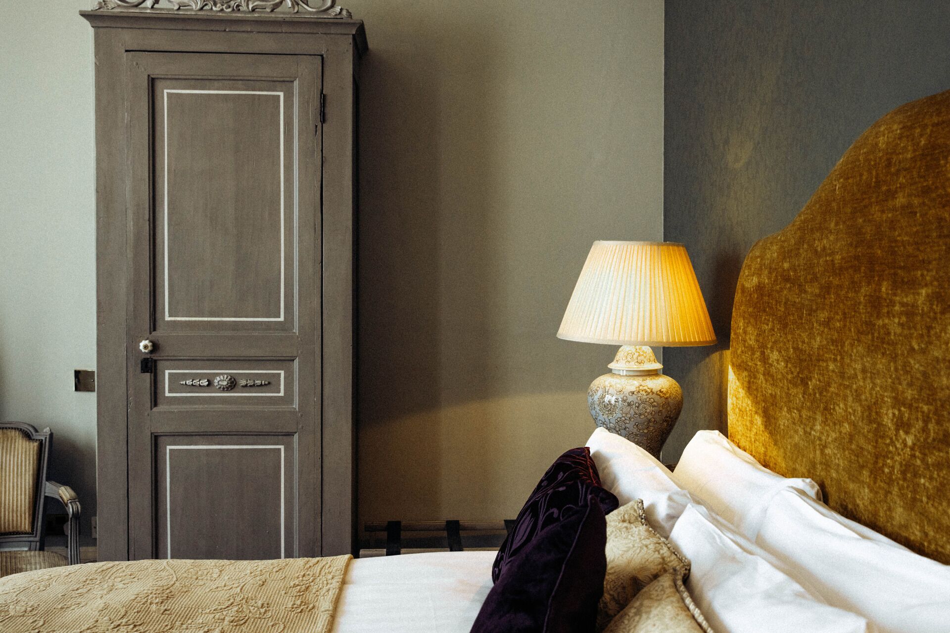Une chambre d’hôtel comprenant un lit, une table de chevet avec une lampe, une armoire et une chaise.