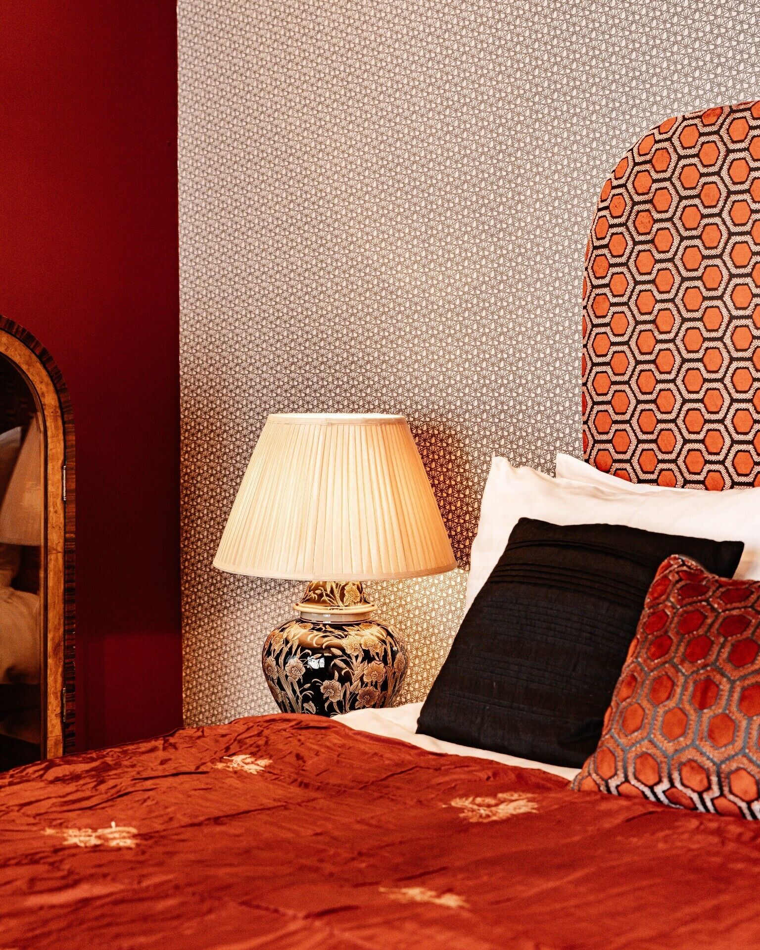 Un dormitorio con colcha roja, pared estampada, lámpara decorativa y espejo.