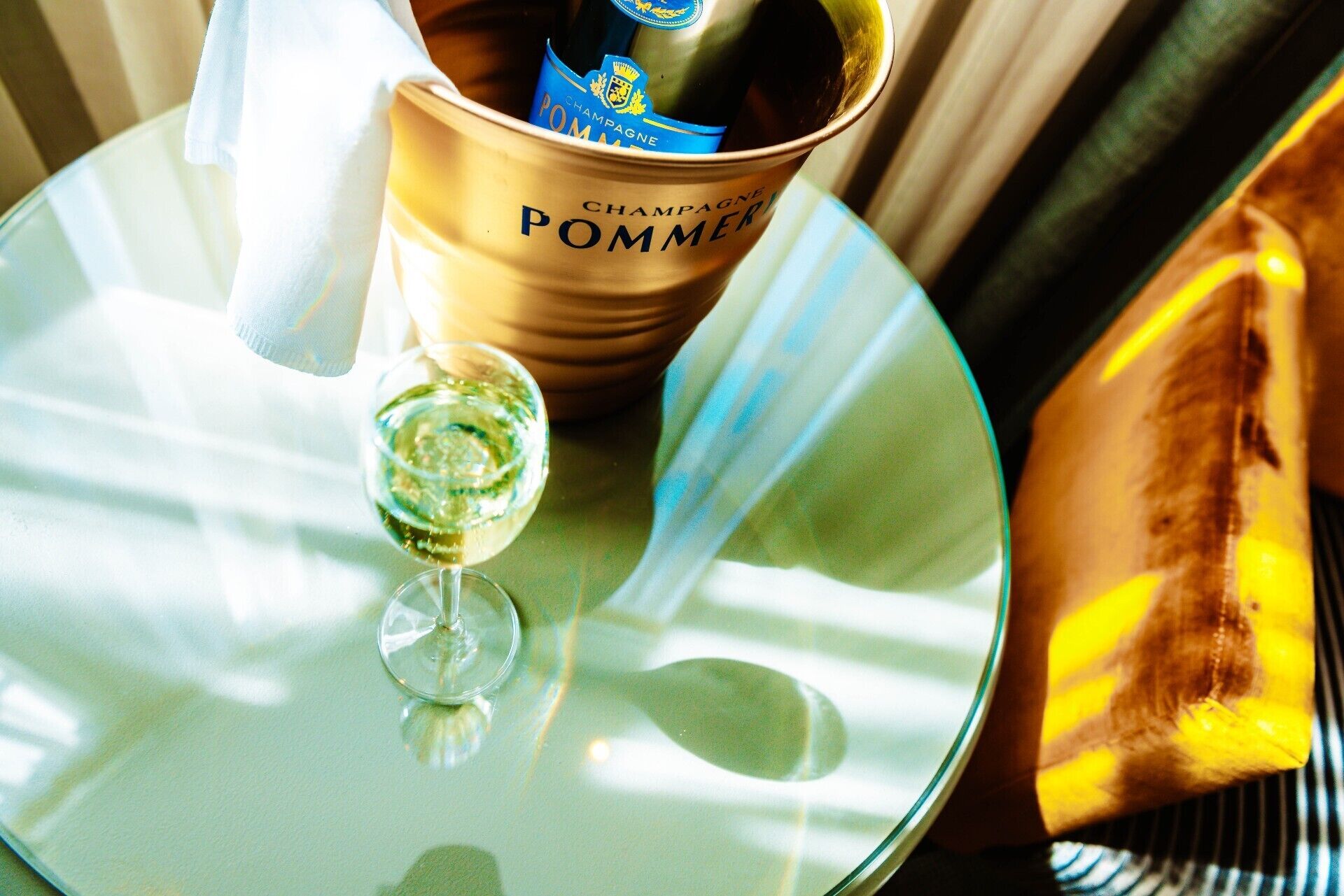A champagne bottle in a branded container, a glass of champagne, and a plate on a table.