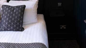 Une chambre d’hôtel avec une tête de lit noire, du linge de lit blanc et trois œuvres d’art florales encadrées accrochées au mur.