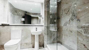 Un baño moderno con inodoro, lavamanos sobre pedestal y ducha con mampara de vidrio.