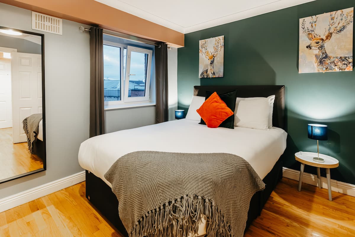 Une chambre avec un grand lit, une fenêtre avec des rideaux, un miroir et deux tableaux accrochés au mur.