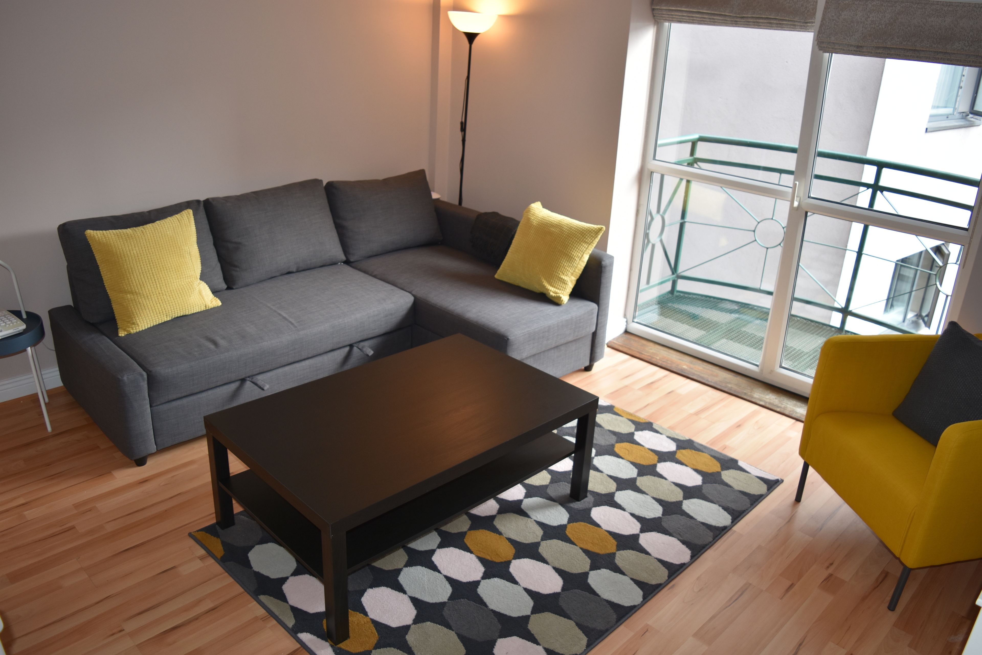 Una sala de estar moderna con un sofá gris, cojines amarillos, una mesa de centro de madera y una alfombra estampada.
