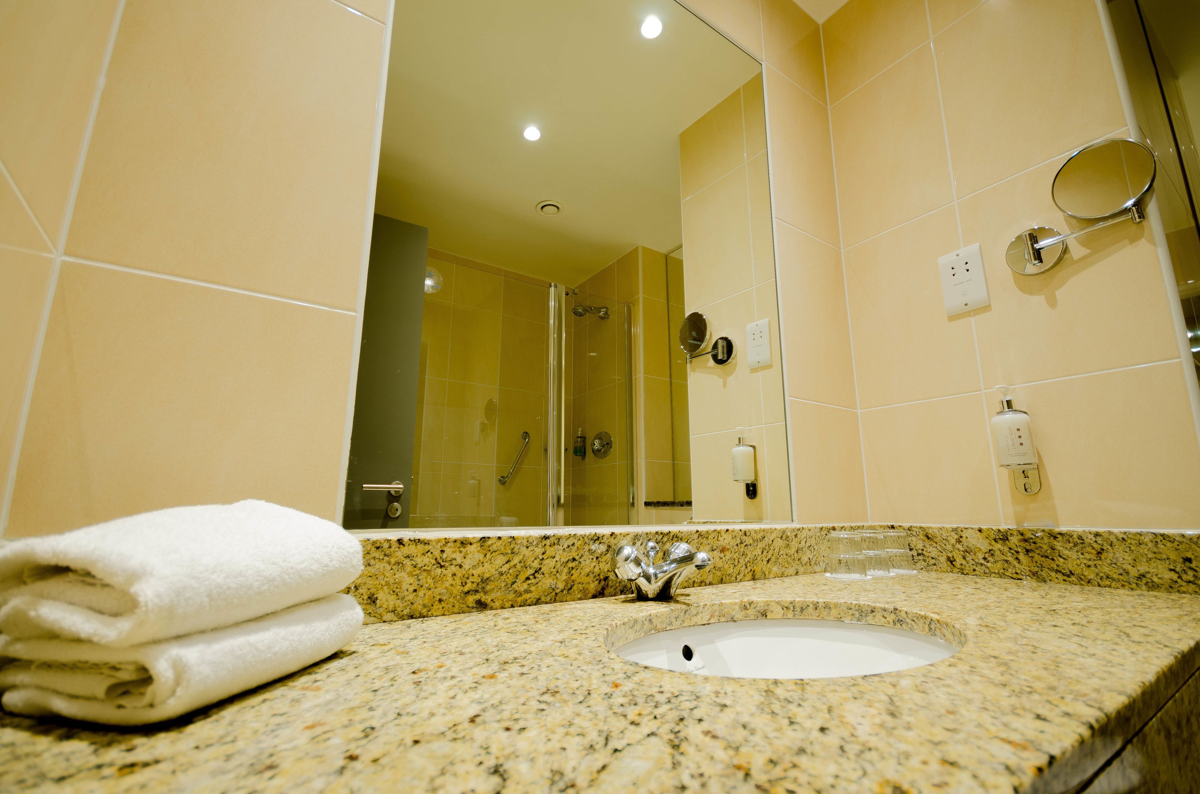 Un baño con lavamanos, espejo y mampara de vidrio.