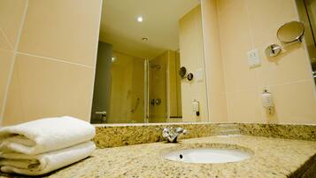 Un baño con lavamanos, espejo y mampara de vidrio.