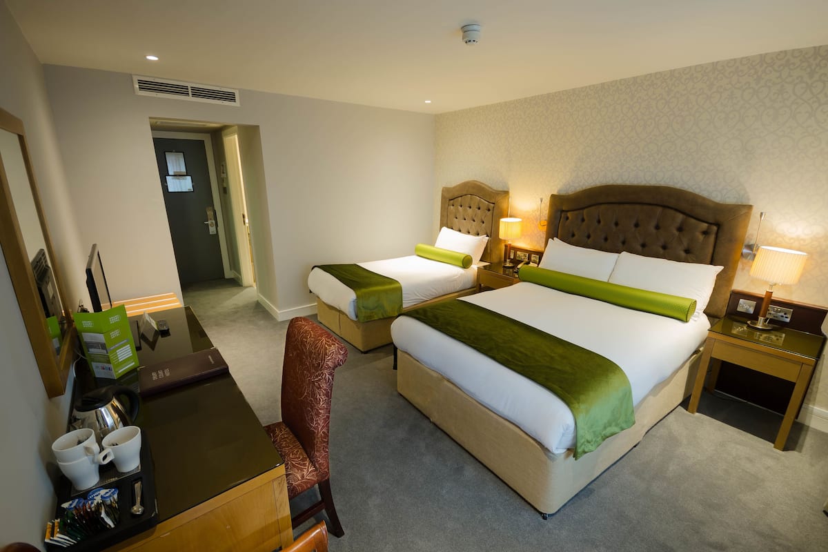 Une chambre d’hôtel avec deux lits, un bureau avec une chaise et une petite table avec une lampe.