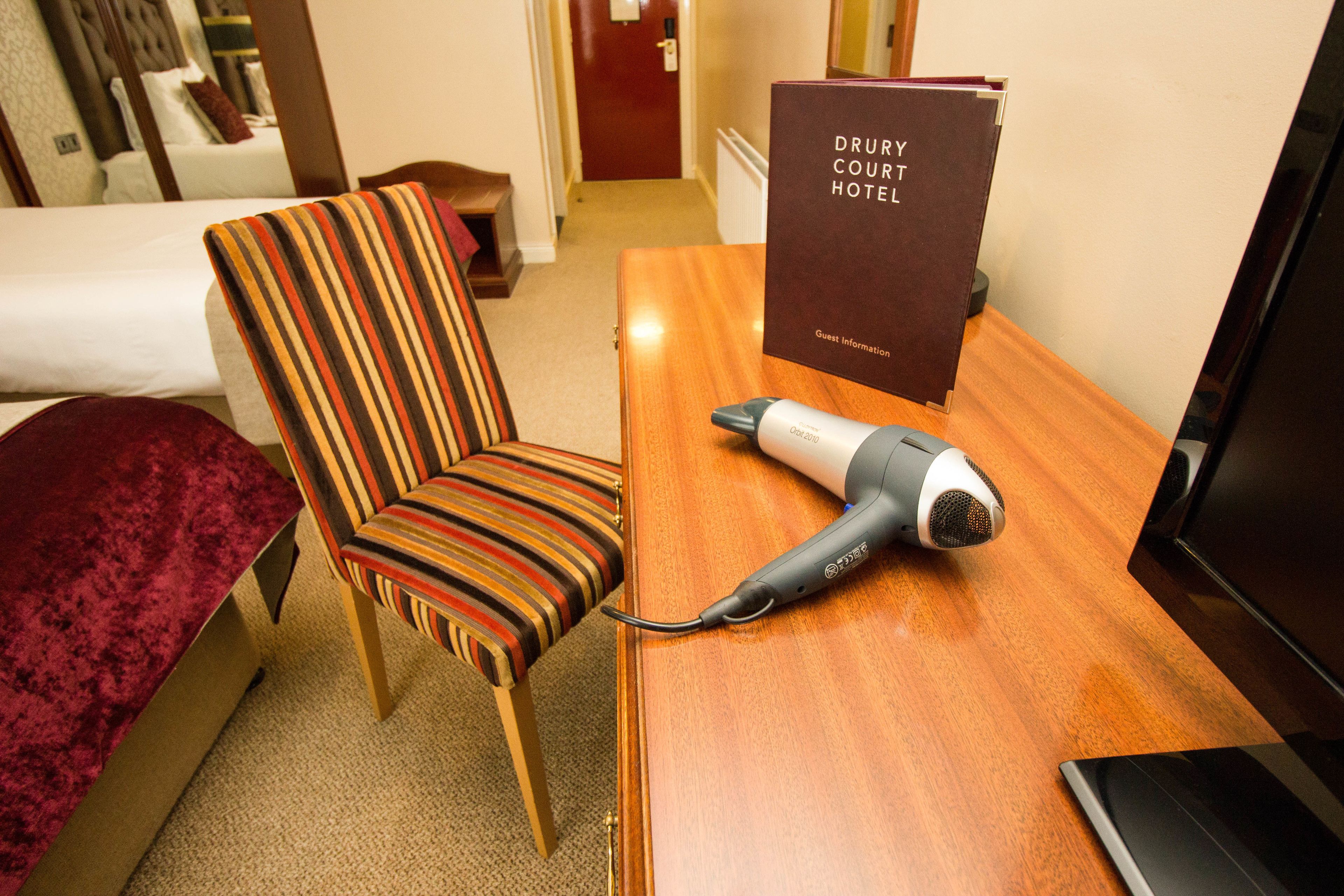 A hotel room with a bed, a striped armchair, a hairdryer, and a sign with the hotel name.
