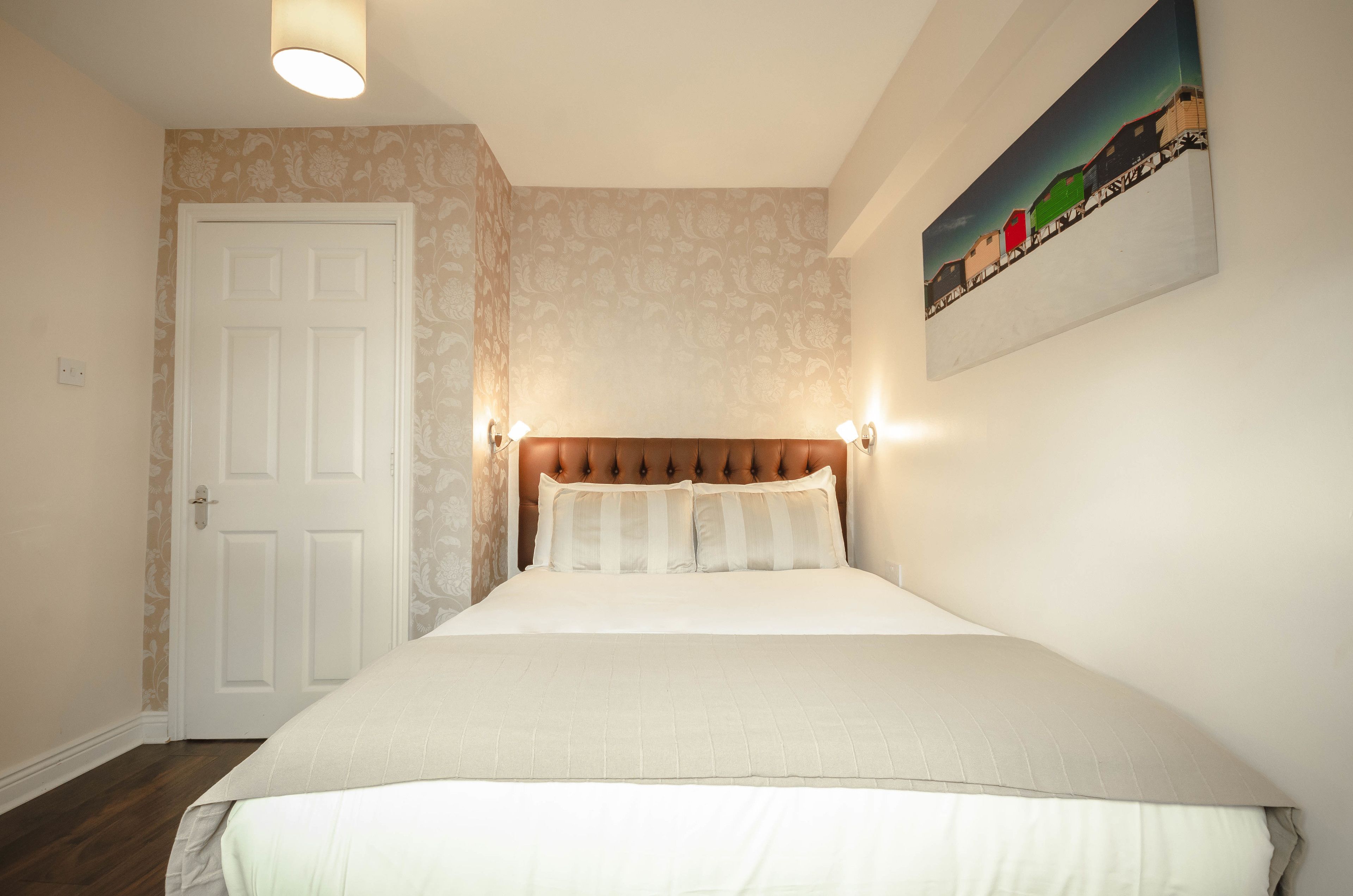 A bedroom with a tufted headboard, a white bedspread, and a painting of a train on the wall.
