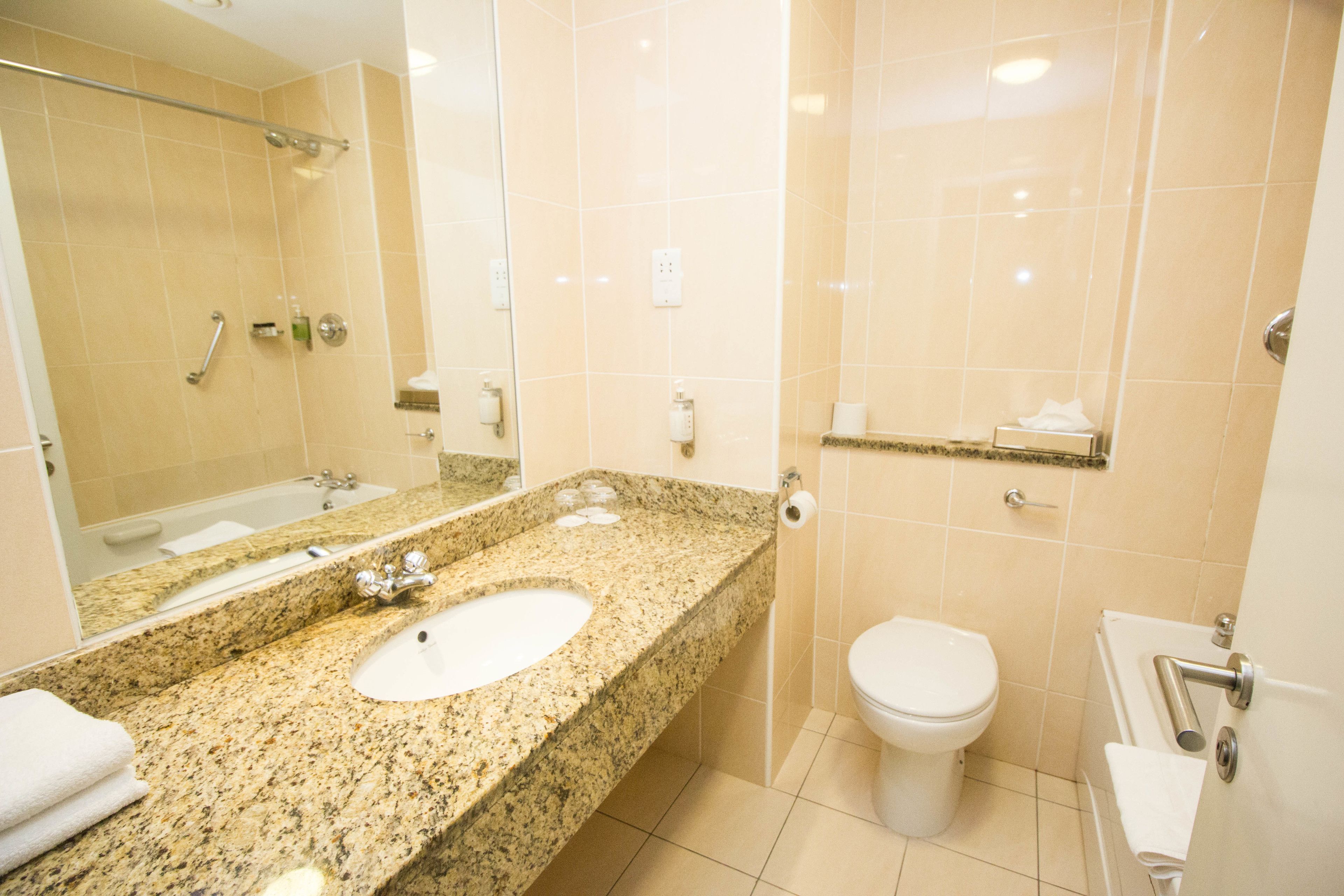 A bathroom with a granite countertop sink, a mirror, a toilet, and a shower area.