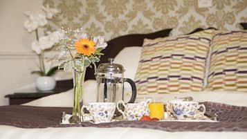 Een netjes opgemaakte ontbijttafel in een kamer, met een bloemenvaas, een koffiepot en kopjes.