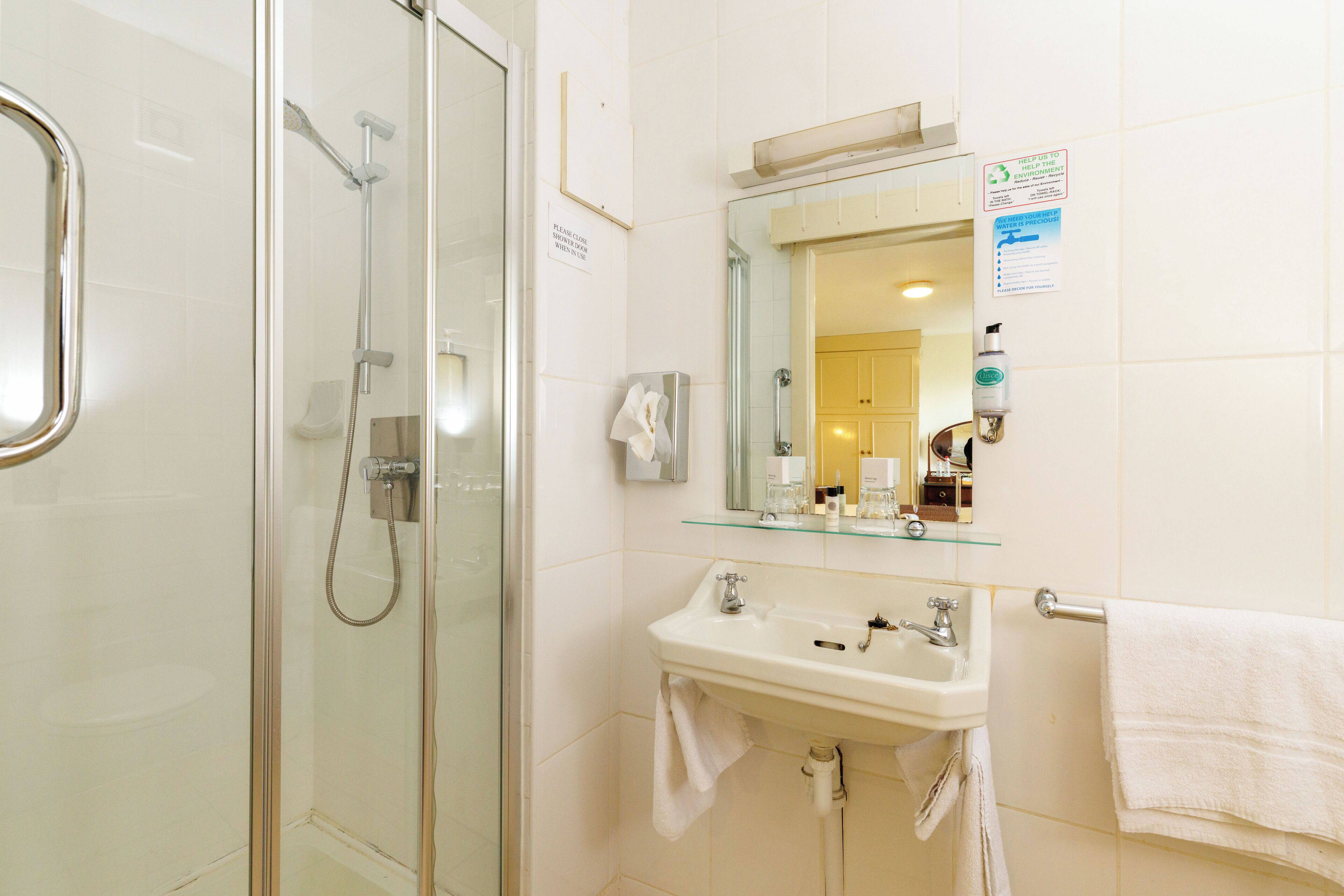 A modern bathroom with a glass-enclosed shower, a white sink with a mirror above it, and a towel rack.