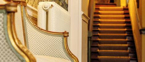 A grand staircase with ornate railings and a plush, upholstered bench with a patterned backrest.