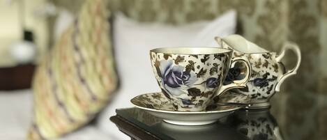 Un juego de té sobre una superficie reflectante, probablemente una mesa, con un cojín estampado y una cama al fondo.
